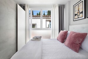 A bedroom with a bed, pillows, a window, and a painting.