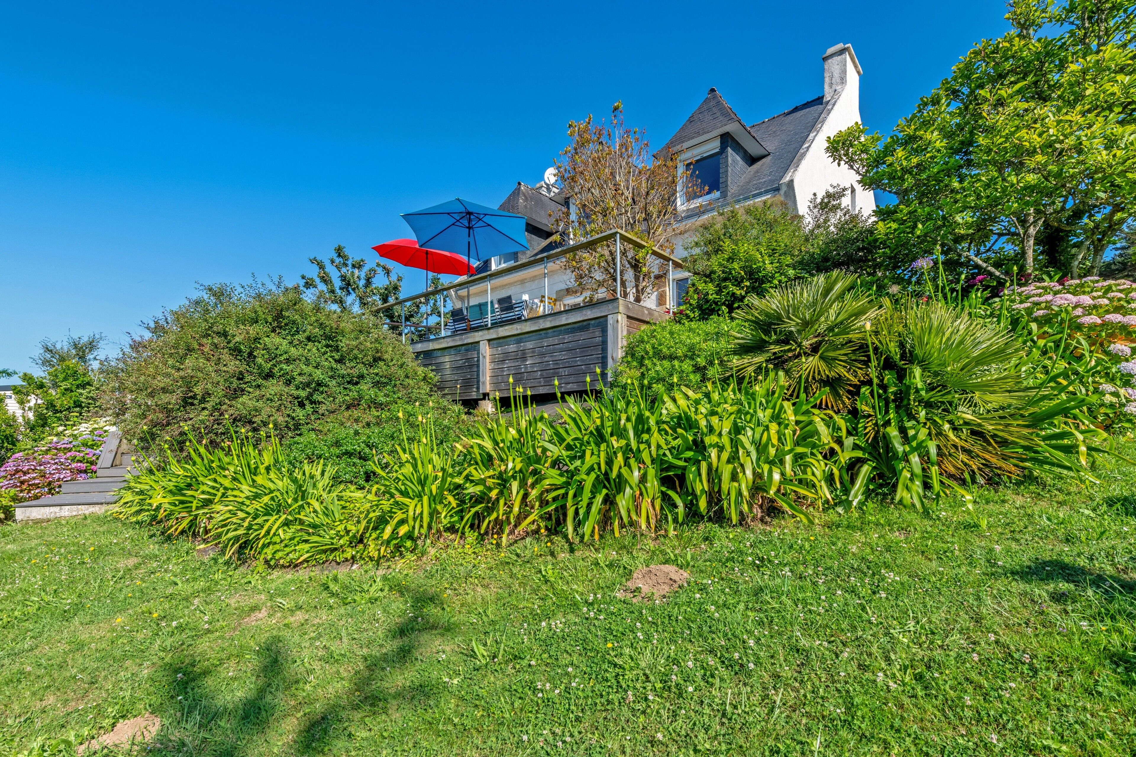 Une maison avec un grand jardin, une terrasse agrémentée de parasols et une cheminée bien visible.