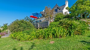 Uma casa com um jardim grande, um alpendre com guarda-sóis e uma chaminé visível.