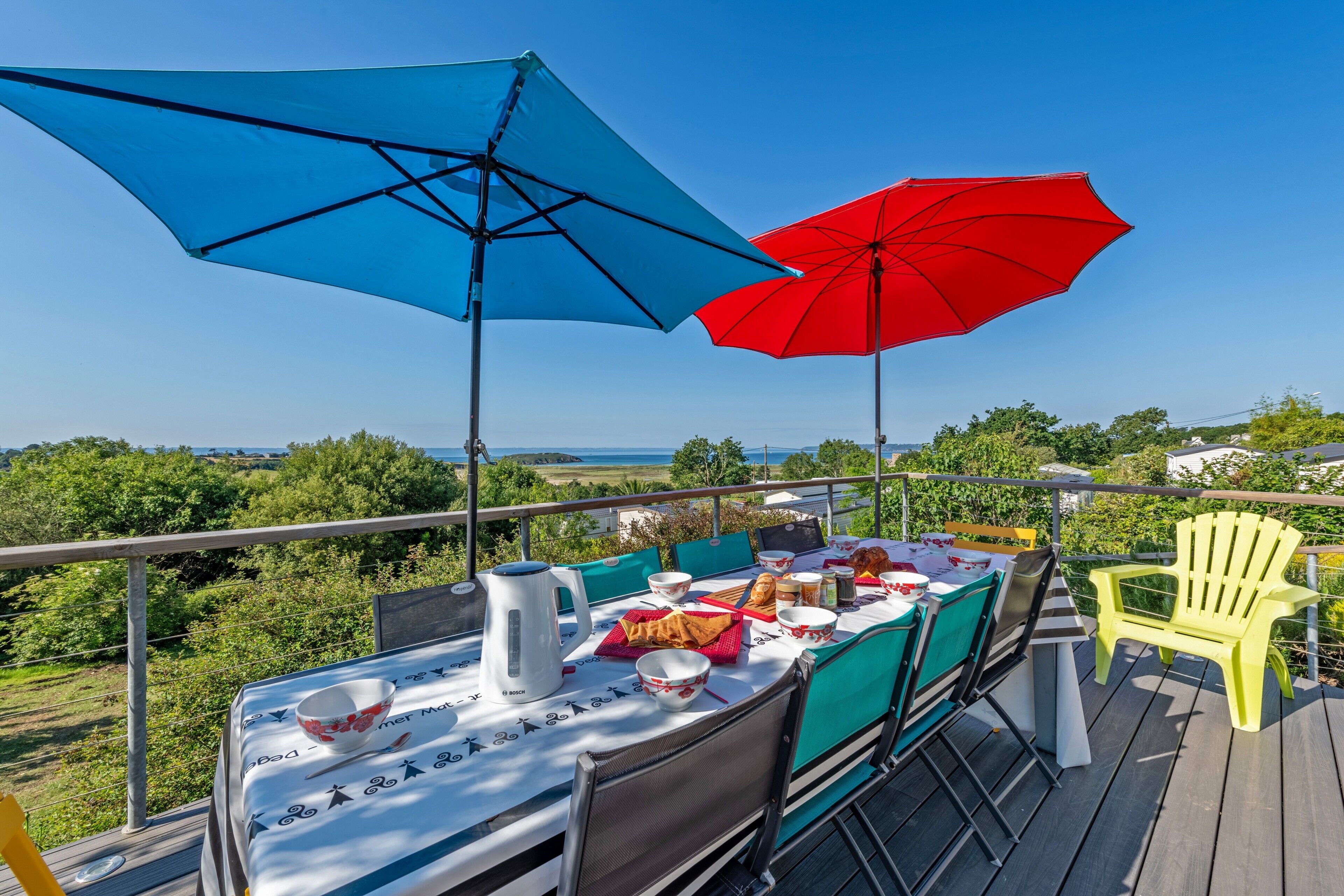 Une terrasse avec une table dressée pour le repas, deux parasols et une chaise jaune.