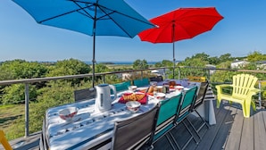 Um terraço com mesa posta para refeições, dois guarda-sóis e uma cadeira amarela.