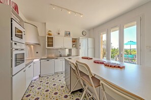 Une cuisine moderne avec des meubles blancs, un four encastré, un évier et un coin repas avec des chaises.