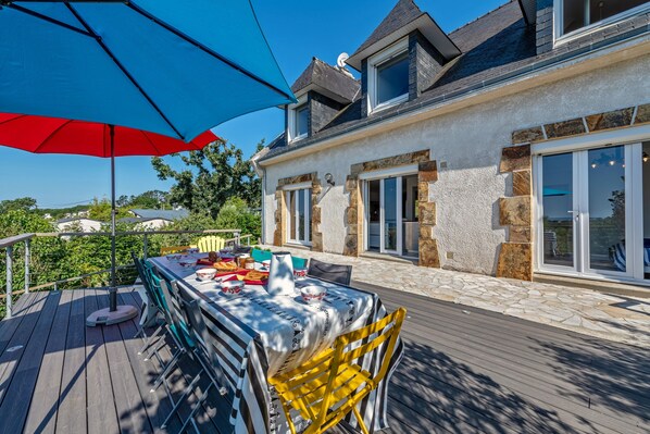 Une terrasse avec une table, des chaises et un parasol rouge.
