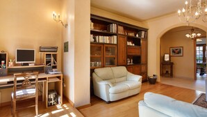 A living room with a desk, computer, bookshelves, two white sofas, and a chandelier.