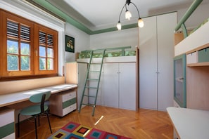 Une chambre avec un lit superposé, un bureau avec une chaise, une échelle et une fenêtre avec des stores.