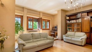 A spacious living room with two sofas, a glass coffee table, a chandelier, and a bookshelf.