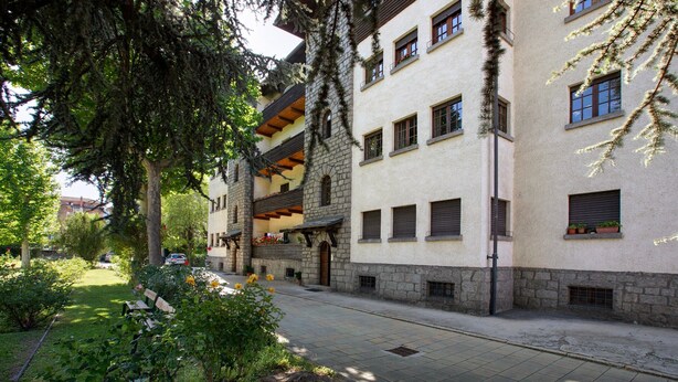 A multi-story building with stone and plaster exteriors, balconies with potted plants, and a paved courtyard with benches.