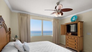 Une chambre avec un grand lit, un ventilateur de plafond, une commode et une vue sur l’océan.