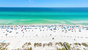 A beach with numerous umbrellas and sun loungers, a clear blue sky, and the ocean.