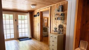 A wooden interior with a white dresser, a trash bin, and a door leading to a kitchen area.