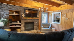 A cozy living room with a stone fireplace, a television mounted above it, and a comfortable seating area.