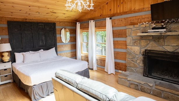 A cozy bedroom with a large bed, a stone fireplace, and a television on a stone shelf.