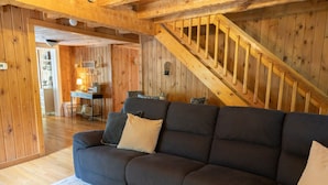 A cozy room with a dark sofa, a wooden staircase, and a small desk with a lamp.