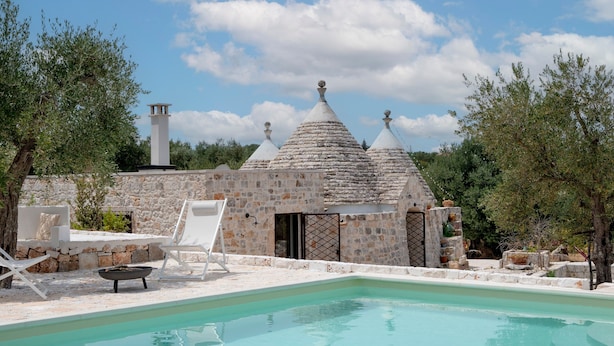 A stone building with conical roofs, a swimming pool, and outdoor seating.
