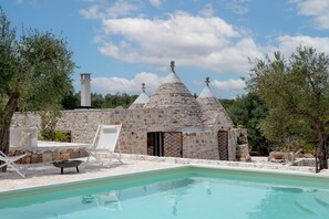 A stone building with conical roofs, a swimming pool, and outdoor seating.