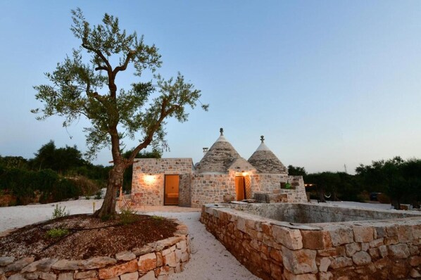 A stone building with a tree in front, a pathway, and a small structure with a dome roof.