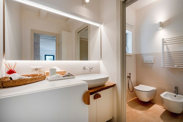 Une salle de bain moderne avec un grand miroir, un lavabo blanc, un plan de toilette en bois, un bidet et un porte-serviettes.