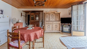 A room with a wooden ceiling, a dining table with a red tablecloth, wooden chairs, a cabinet with glass doors, and a television. - Holiday Home 'Blanche Neige Mimizan' with Private Terrace and Shared Garden (Mimizan)