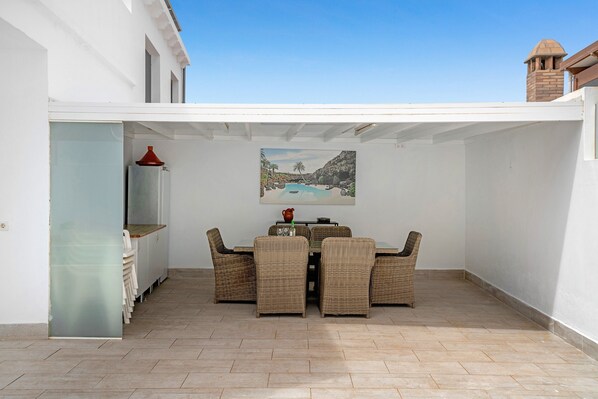 A covered patio with wicker furniture, a painting, and a tiled floor.