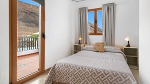 A bedroom with a bed, a window, curtains, a nightstand, and a balcony.
