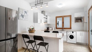 A modern kitchen with a stainless steel refrigerator, a built-in washing machine, and a large island with bar stools.