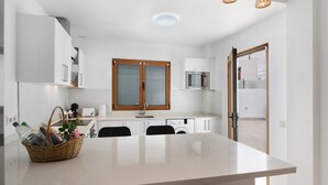 A modern kitchen with white cabinetry, a wooden-framed window, a microwave, and a sink.