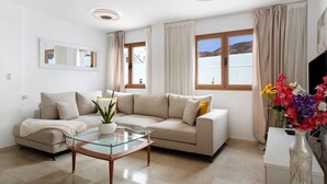 A living room with a sofa, glass coffee table, and a vase of flowers.