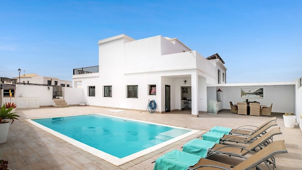 A modern white building with a swimming pool and lounge chairs.
