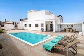 A modern white building with a swimming pool and lounge chairs.