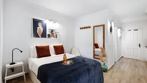 A bedroom with a bed, bedside table, lamp, artwork, and a mirror.