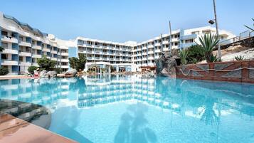 Un hotel con piscina, varios balcones y una zona ajardinada con rocas y plantas.