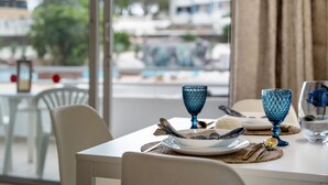 A dining table set with plates, glasses, and cutlery, with a view of a pool and buildings outside.