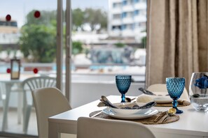Une table à manger dressée avec des assiettes, des verres et des couverts, donnant sur une piscine et des bâtiments à l’extérieur.