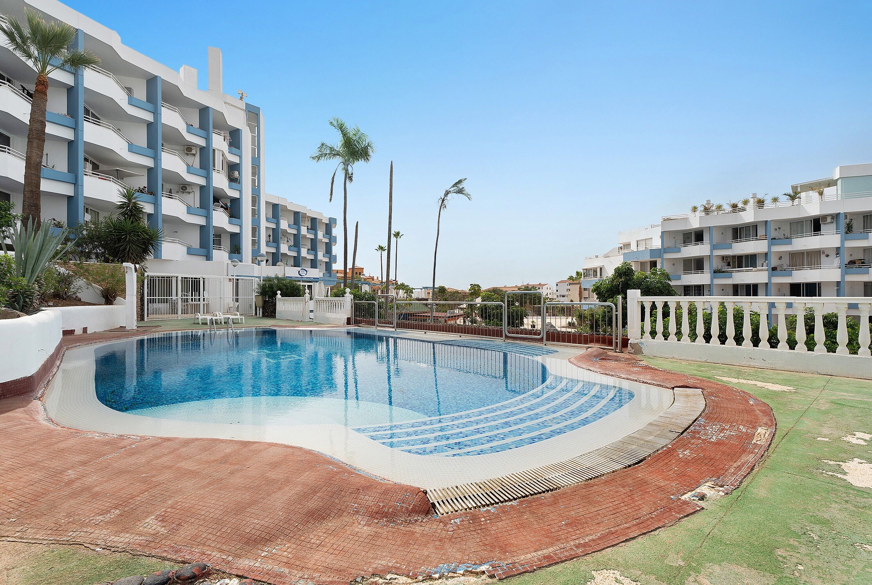 Una piscina de vora corbada, envoltada per una terrassa de maó i una tanca blanca.