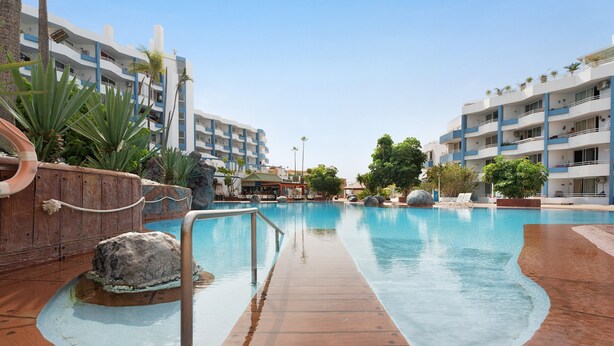 A swimming pool with a wooden deck, surrounded by multi-story buildings with balconies.