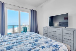 Ein Schlafzimmer mit Bett, Fernseher, Kommode und einem Balkon mit Meerblick.