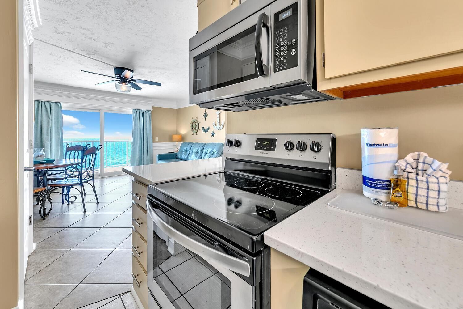 A modern kitchen with a microwave, stove, and oven. There is a dining area with a table and chairs, and a view of the ocean through large windows.