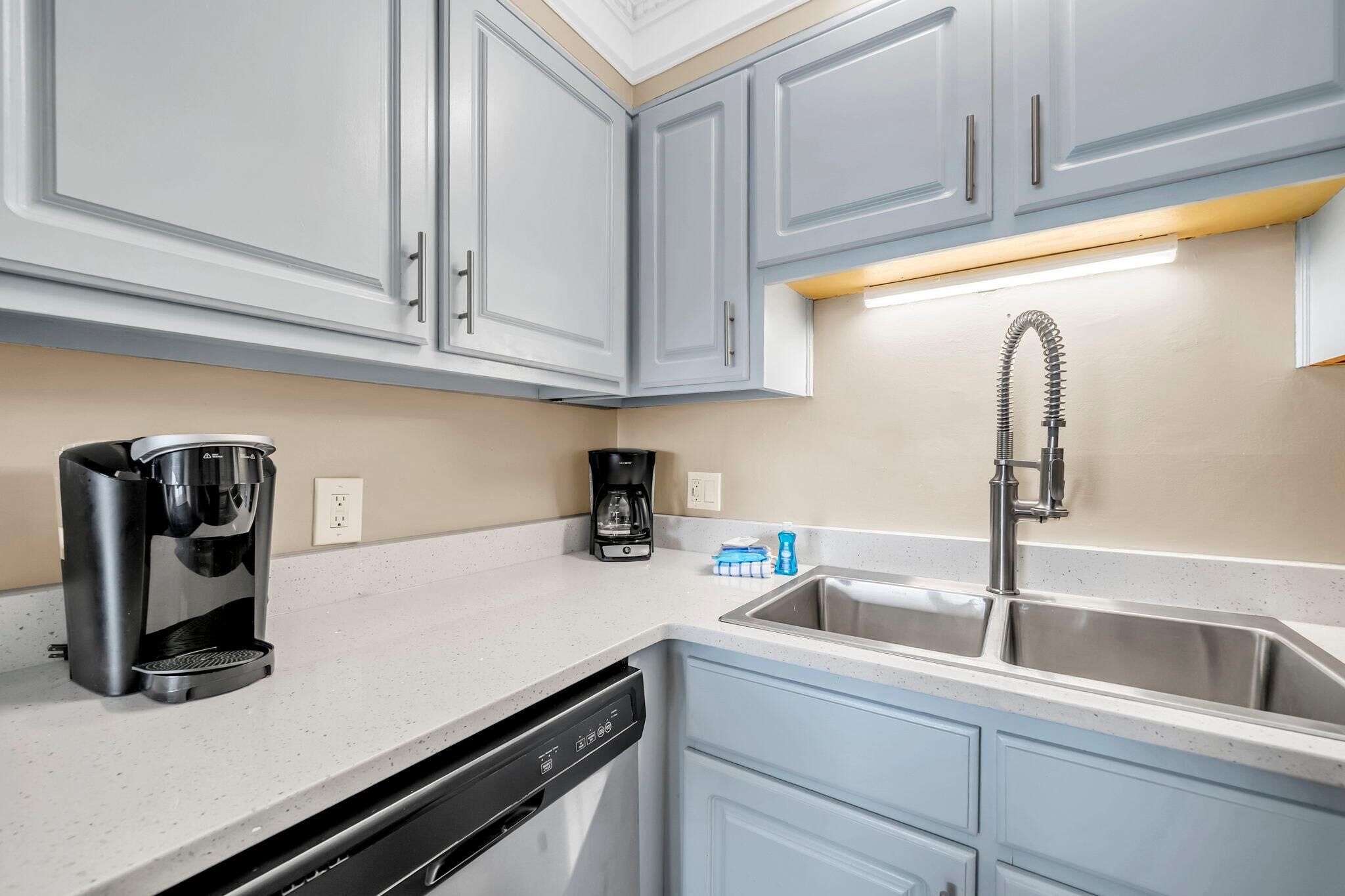 A kitchen with grey cabinets, a coffee maker, a dishwasher, and a sink with a faucet.