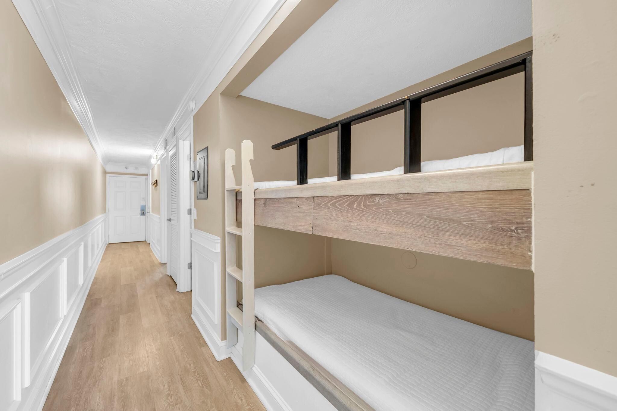 A narrow hallway with bunk beds, white trim, and a wooden floor.