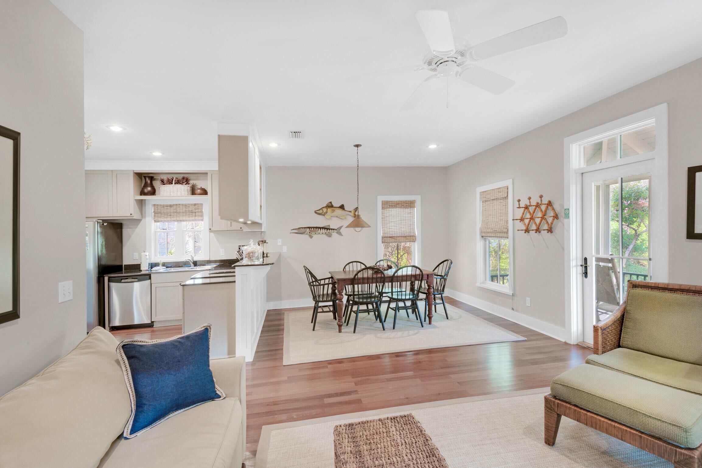 A spacious living room with a sofa, a dining area with a table and chairs, a kitchen with white cabinets, and a ceiling fan.