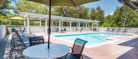 Zona de piscina con un pérgola, sillas de descanso y una mesa con sombrilla.