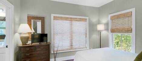 Un dormitorio con cama, cómoda, televisor y ventanas con persianas.
