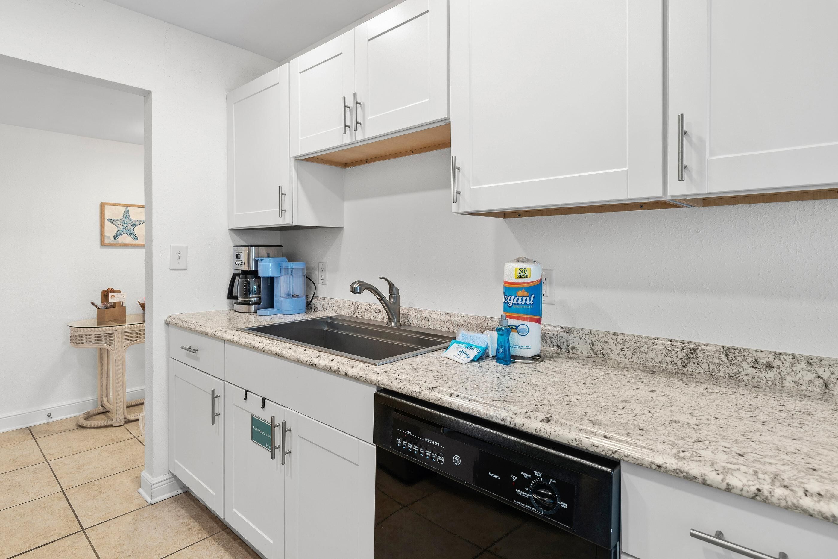 A modern kitchen with white cabinets, a granite countertop, a dishwasher, and a coffee maker.