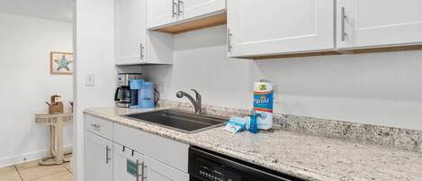 A modern kitchen with white cabinets, a granite countertop, a dishwasher, and a coffee maker.