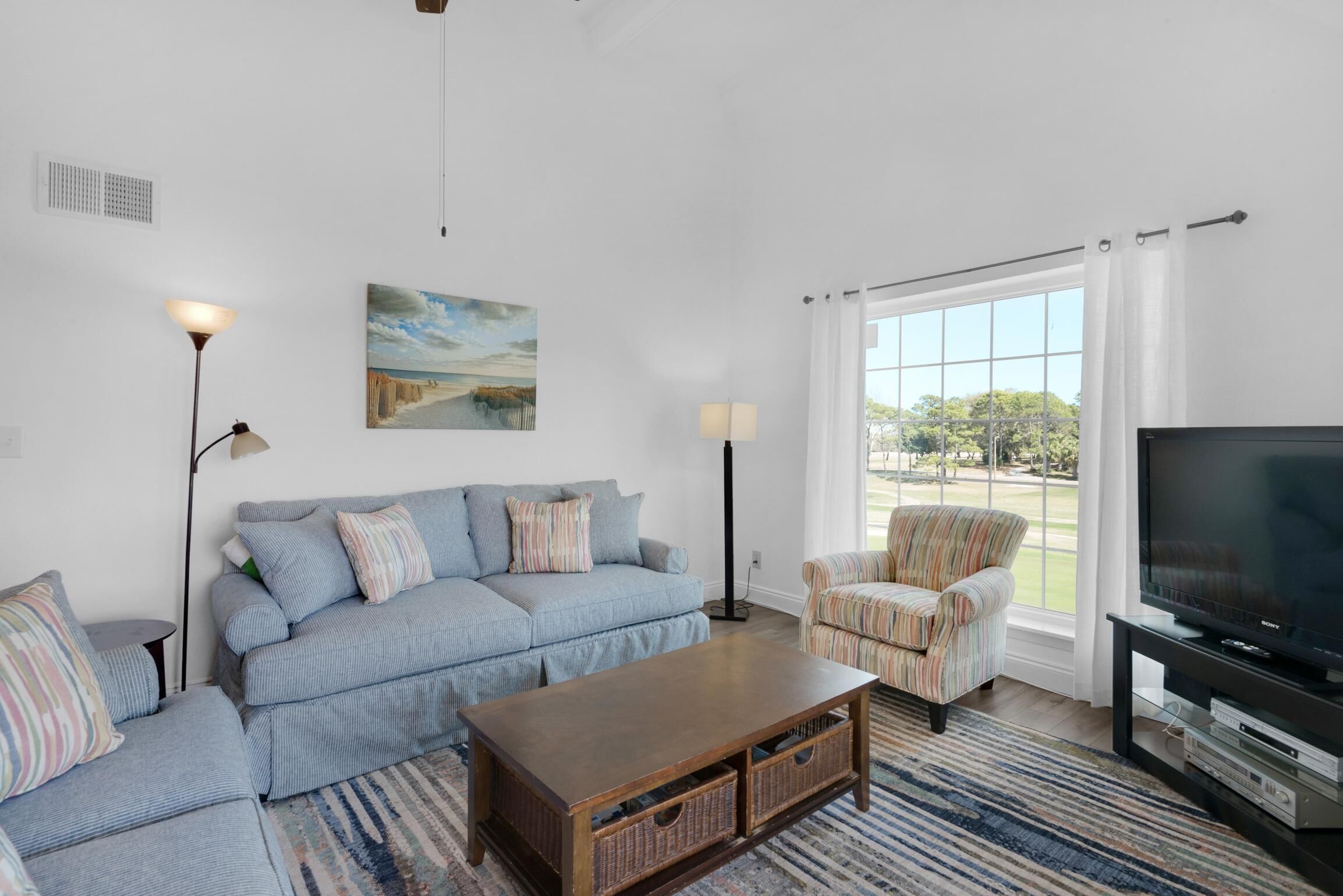 A living room with a sofa, armchair, coffee table, TV, and large windows.