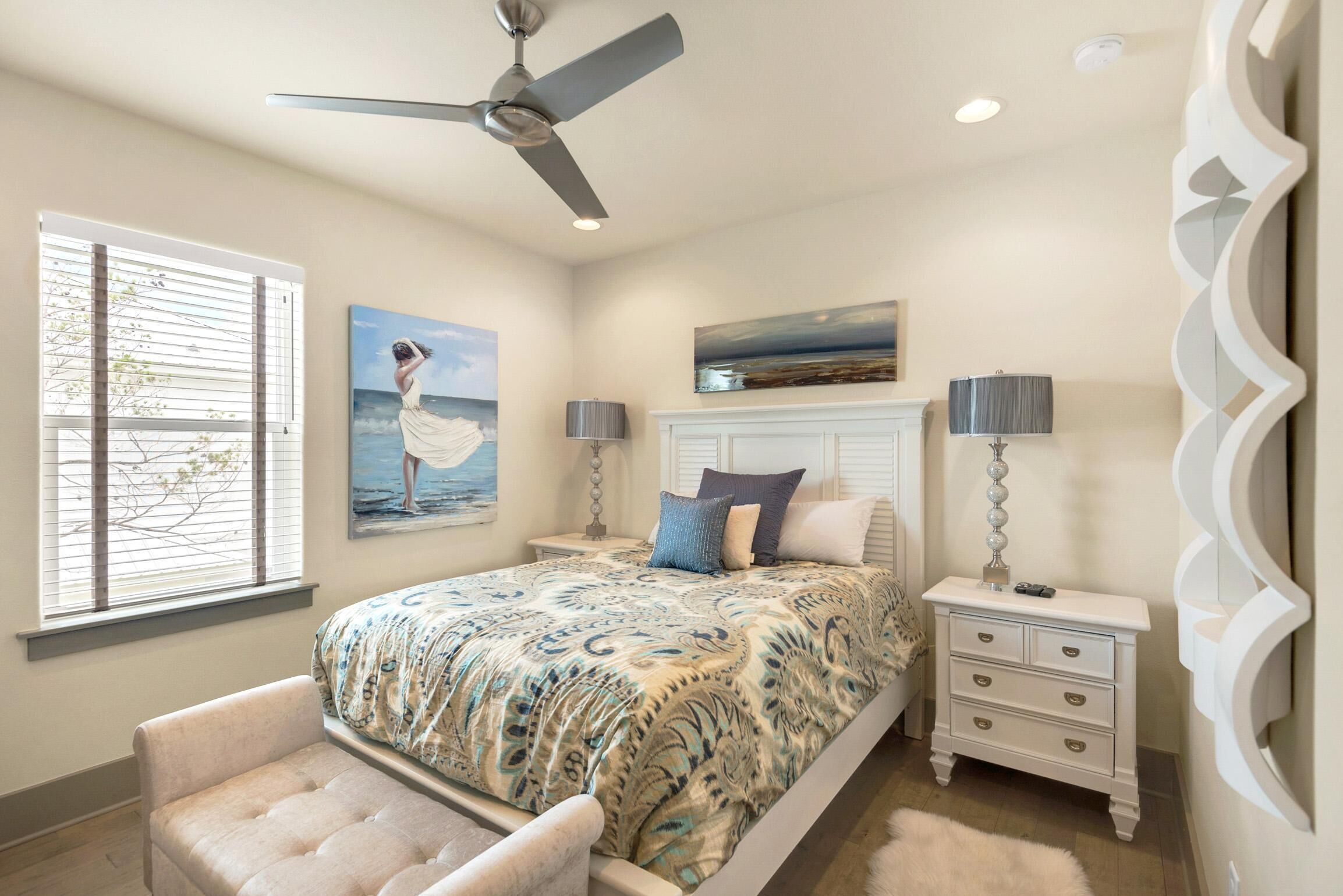 A bedroom with a bed, nightstands, a ceiling fan, and artwork on the walls.