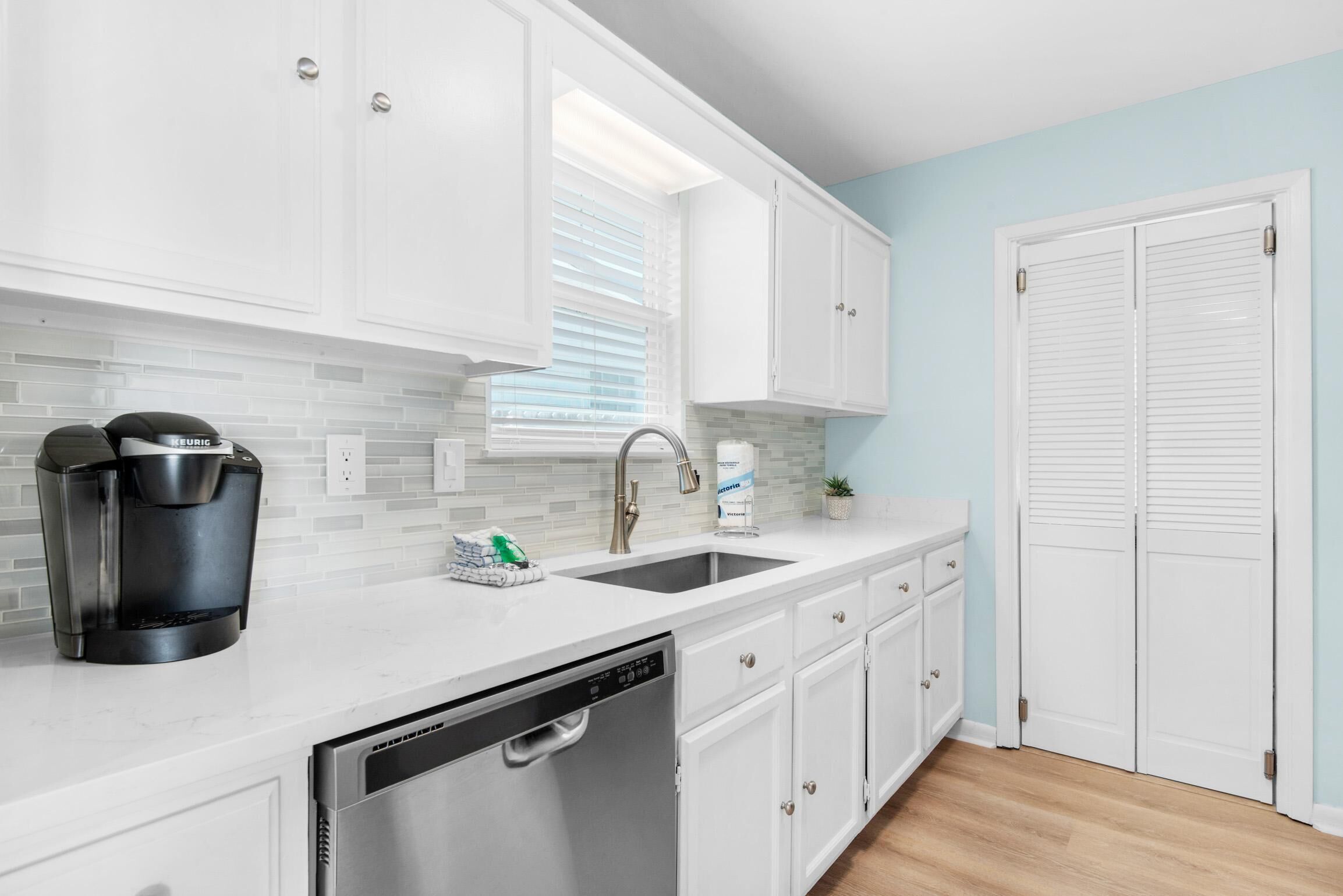 A modern kitchen with white cabinets, a stainless steel dishwasher, a coffee maker, and a sink.