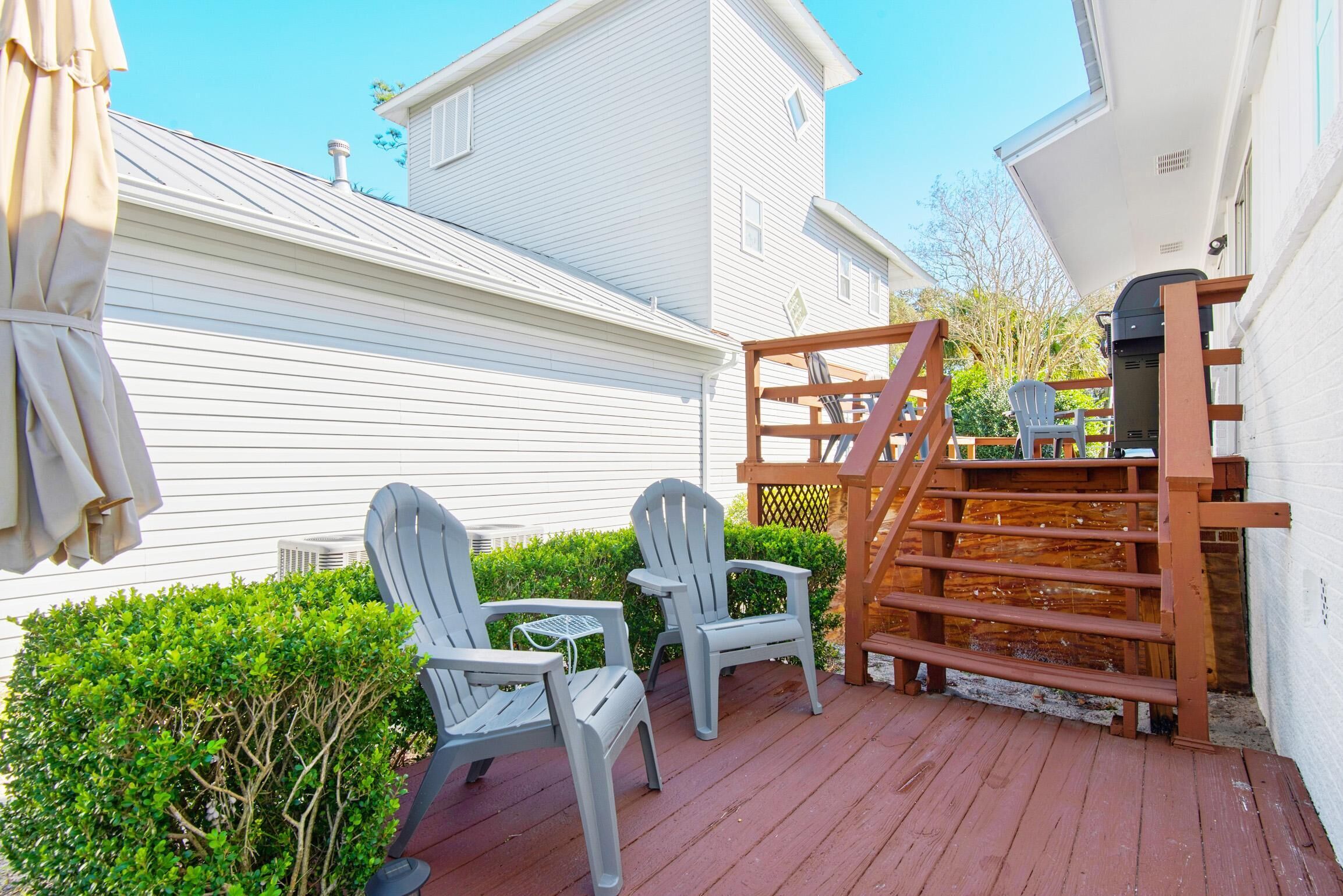 A wooden deck with two chairs and a table, a wooden fence, and a white building in the background.
