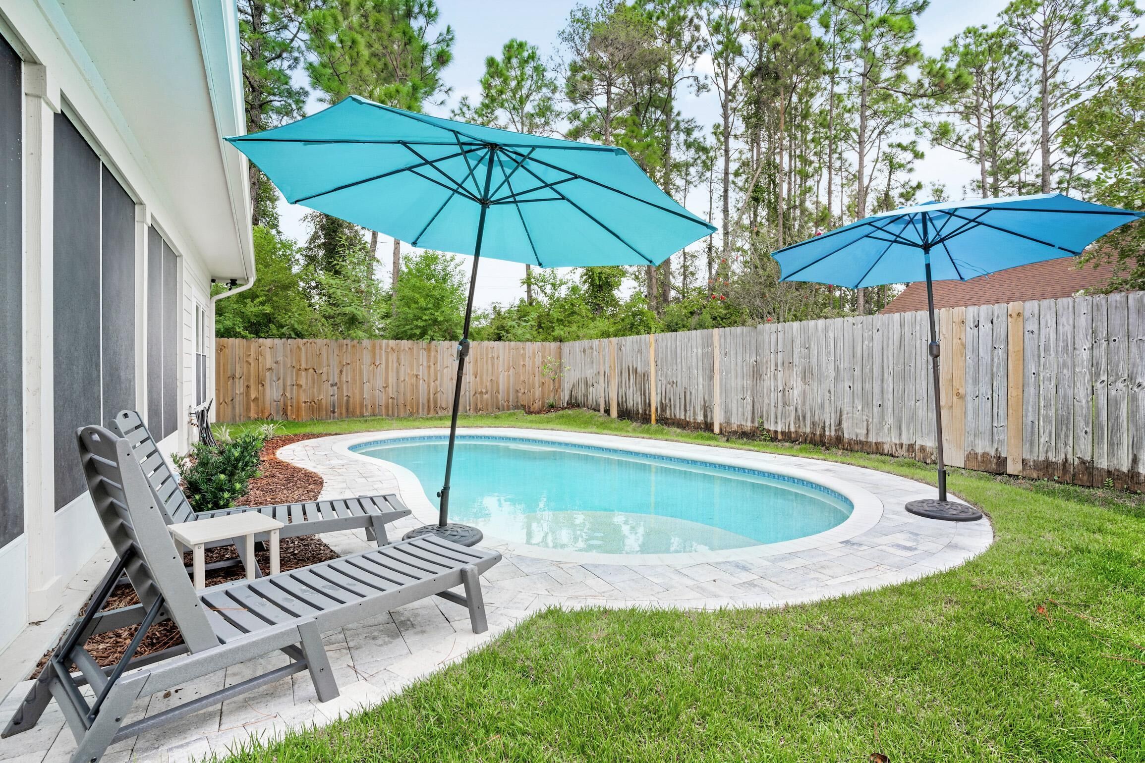 A backyard with a swimming pool, two lounge chairs, and two umbrellas.