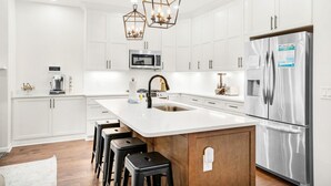 Eine moderne Küche mit weißen Schränken, einem Edelstahlkühlschrank, einer eingebauten Mikrowelle und einer zentralen Kochinsel mit Sitzgelegenheiten.